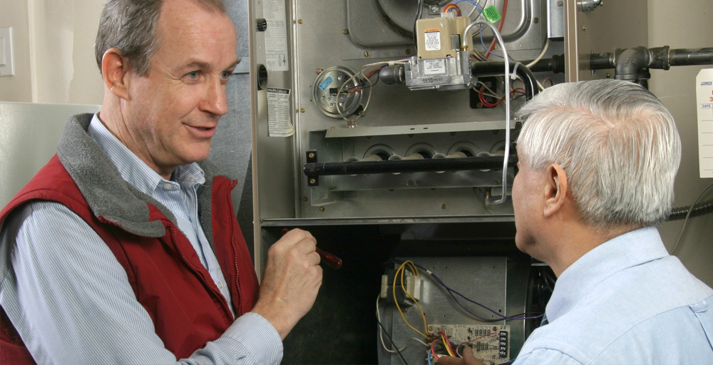 A KLEBS heating advisor explaining the inner workings of a furnace with a customer, in front of his open furnace.